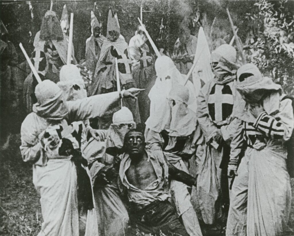 Still from Birth of a Nation showing Ku Klux Klan surrounding a man darkened to appear African American