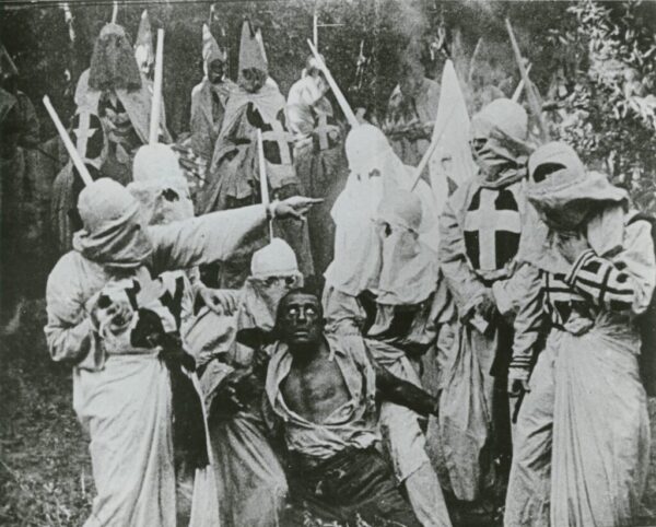 Still from Birth of a Nation showing Ku Klux Klan surrounding a man darkened to appear African American